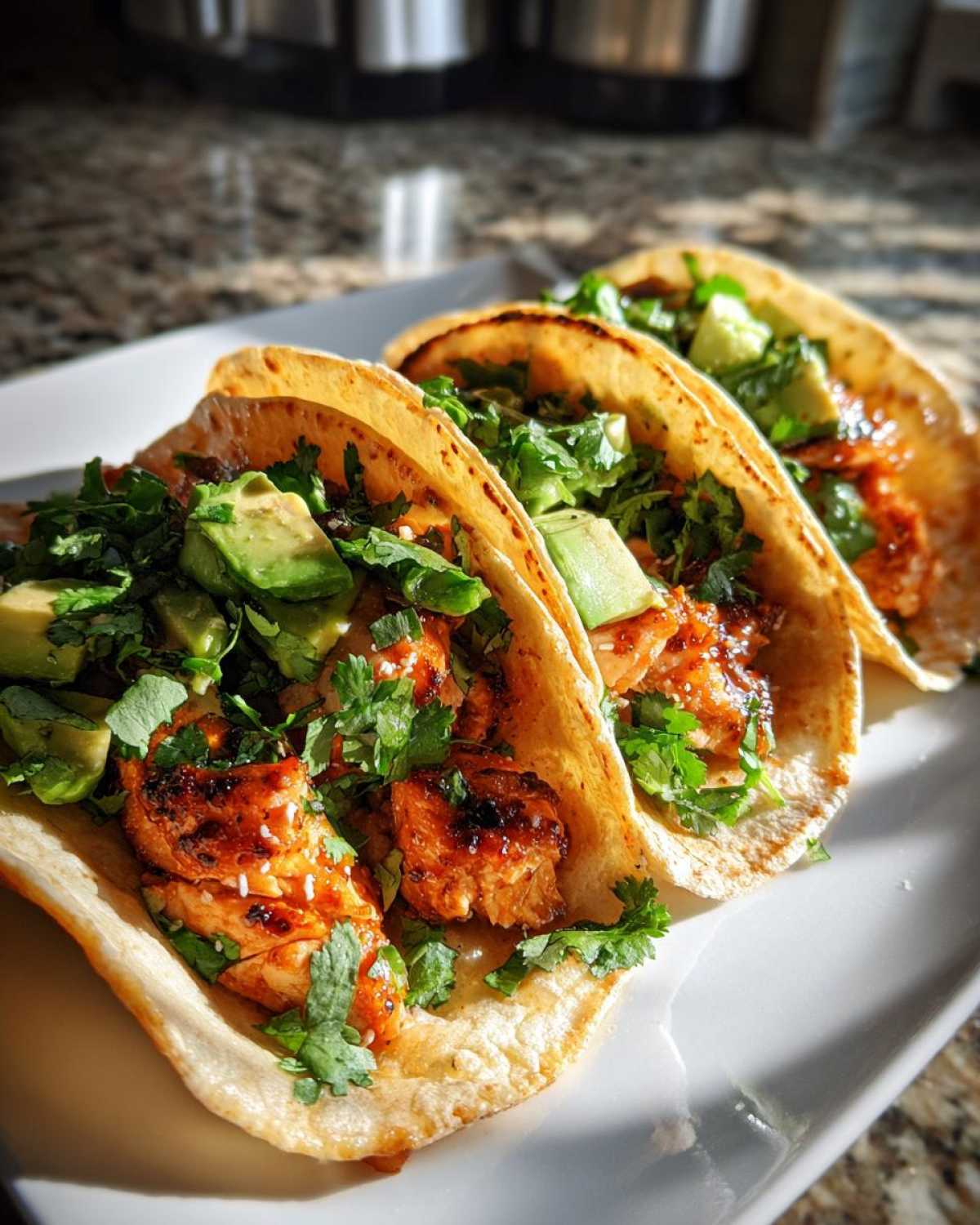 Close-up of three chipotle honey salmon tacos filled with glazed salmon, diced avocado, and fresh cilantro.