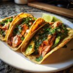 Close-up of three chipotle honey salmon tacos filled with flaked salmon, avocado, and cilantro on a white plate.