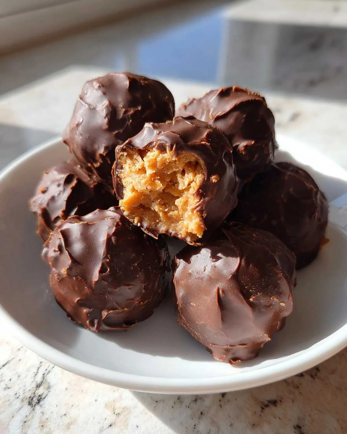 A pile of homemade chocolate covered peanut butter balls, with one bitten open revealing the creamy center.