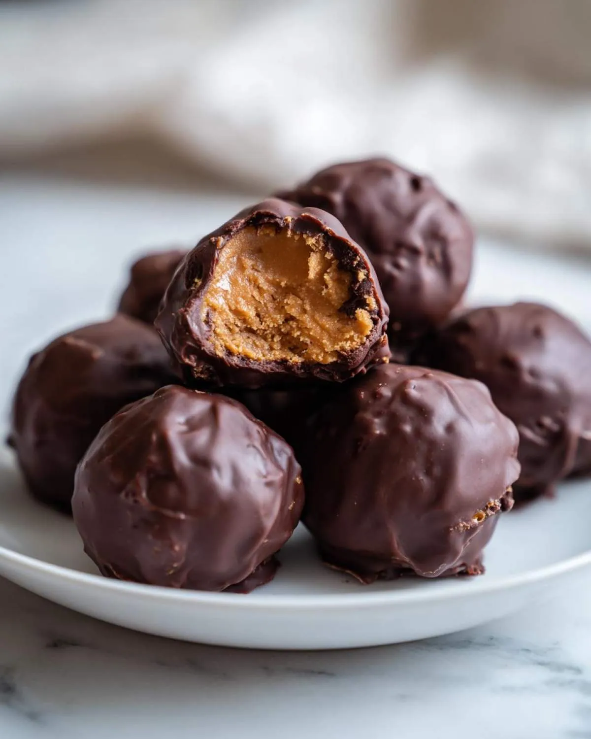 A stack of chocolate-covered peanut butter balls, with one cut in half showing the creamy peanut butter filling.