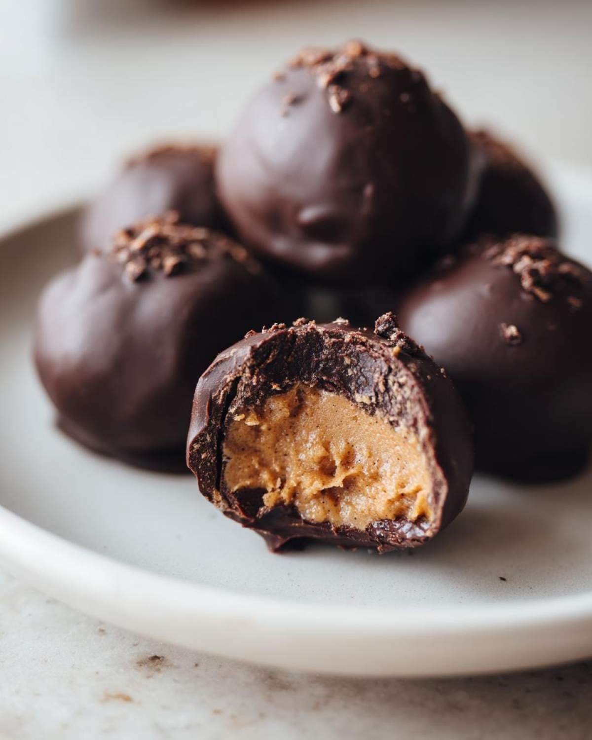 Close-up of chocolate coated peanut butter balls, one cut in half showing the creamy peanut butter filling.