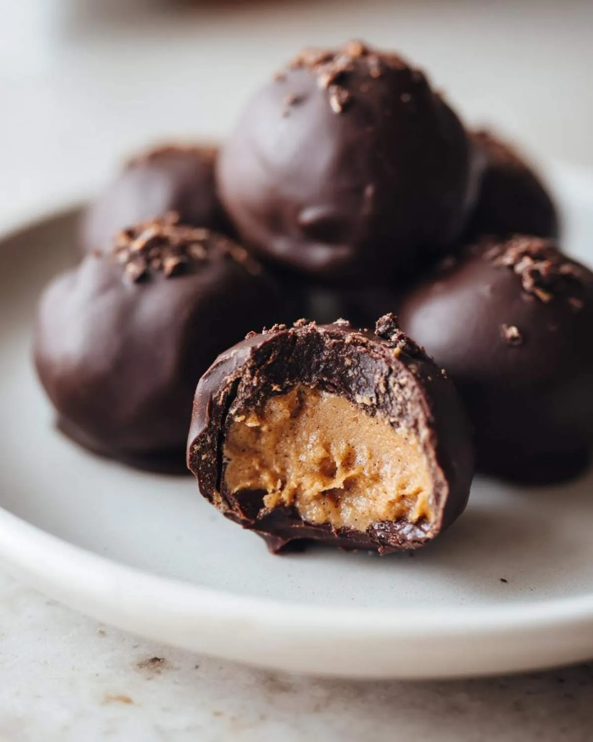 Close-up of chocolate coated peanut butter balls, one cut in half showing the creamy peanut butter filling.