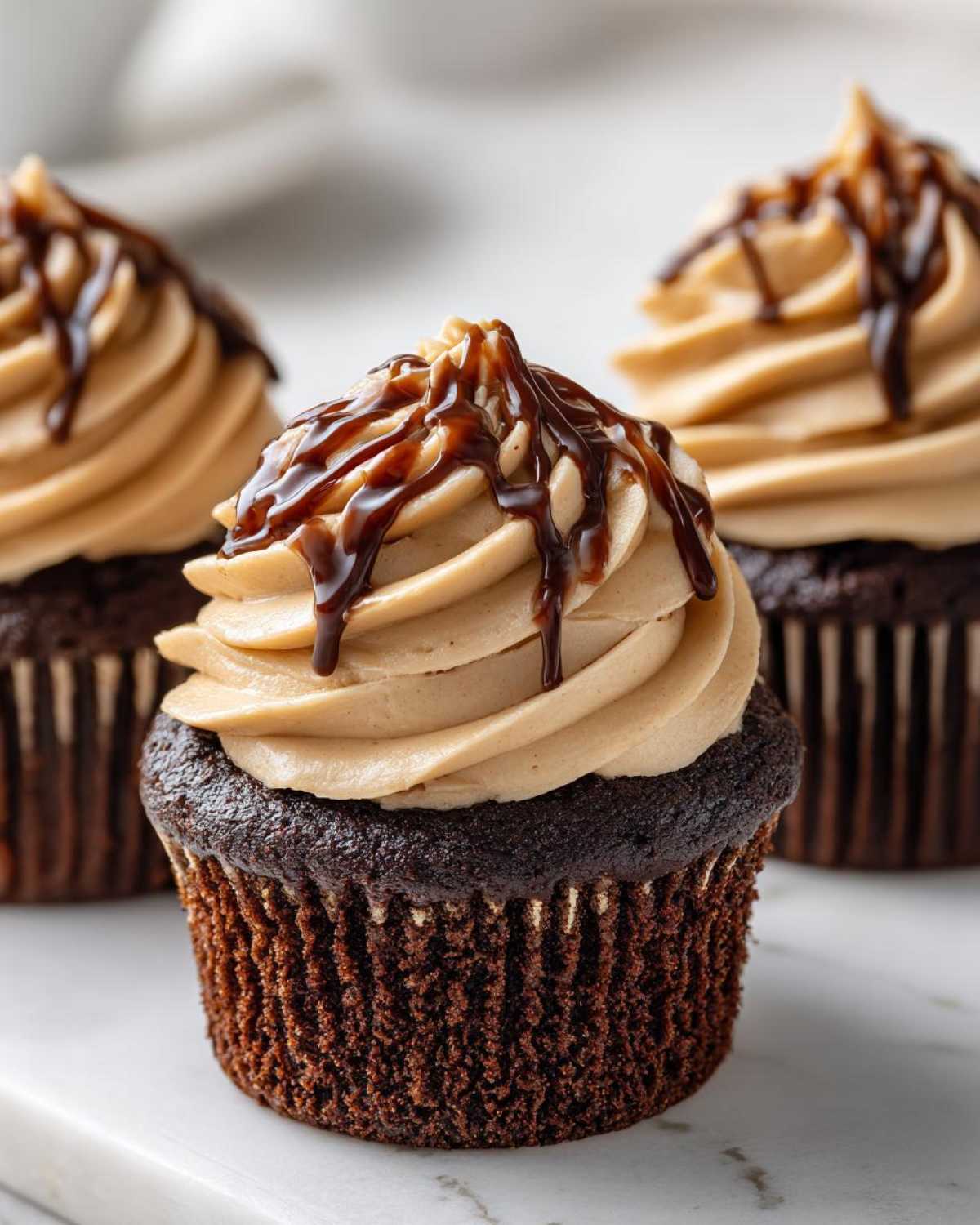A close-up of one of the amazing chocolate tiramisu cupcakes topped with light brown frosting and a dark chocolate drizzle.