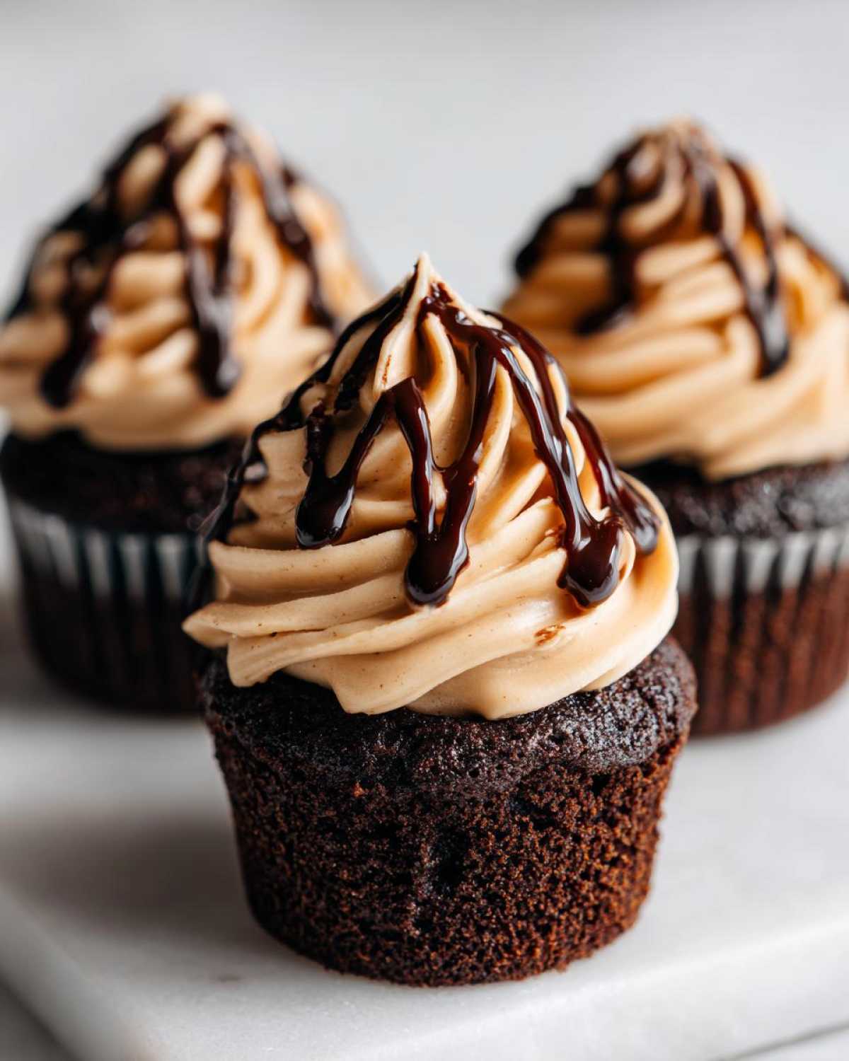 Close-up of a rich chocolate tiramisu cupcakes topped with light brown frosting and a dark chocolate drizzle.