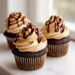 Three decadent chocolate tiramisu cupcakes topped with light brown frosting and drizzled with dark chocolate syrup.