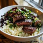 Close-up of a white bowl filled with cilantro lime steak bowls, featuring sliced steak over rice, black beans, and fresh cilantro.