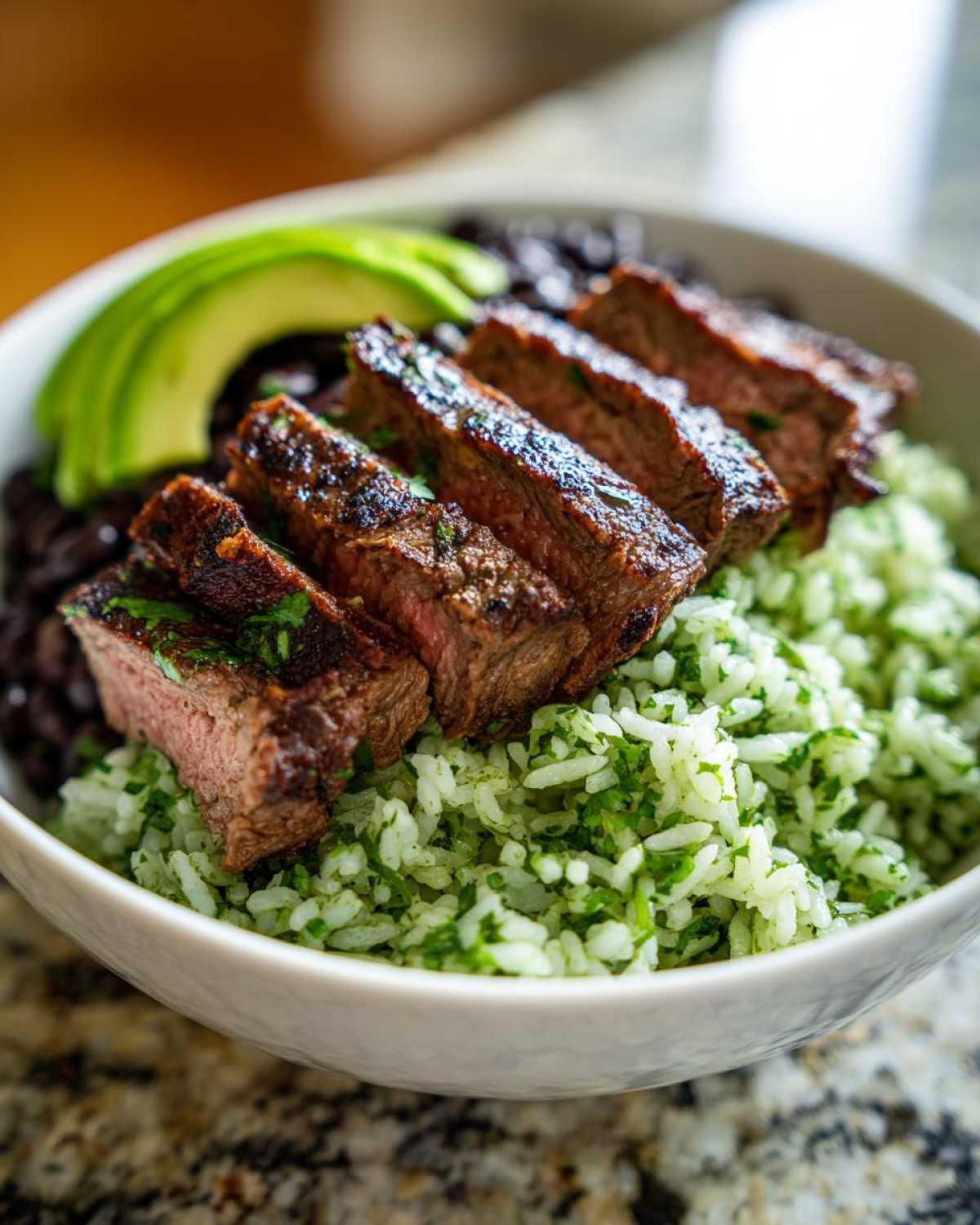 Close-up of sliced steak over cilantro lime rice and black beans in a bowl, part of a cilantro lime steak bowls recipe.