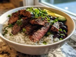 A close-up view of a white bowl filled with cilantro lime steak bowls, featuring sliced steak over white rice, black beans, and avocado slices.