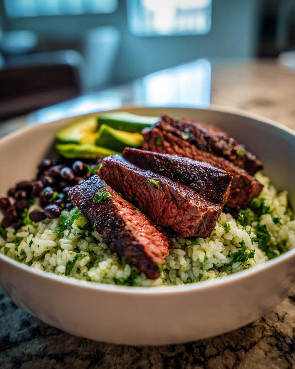 Close-up of a cilantro lime steak bowls featuring sliced medium-rare steak over cilantro rice, black beans, and avocado.