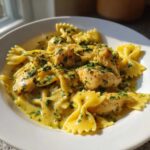 Close-up of cowboy butter lemon bowtie chicken served over farfalle pasta in a rich, yellow sauce, topped with parsley.