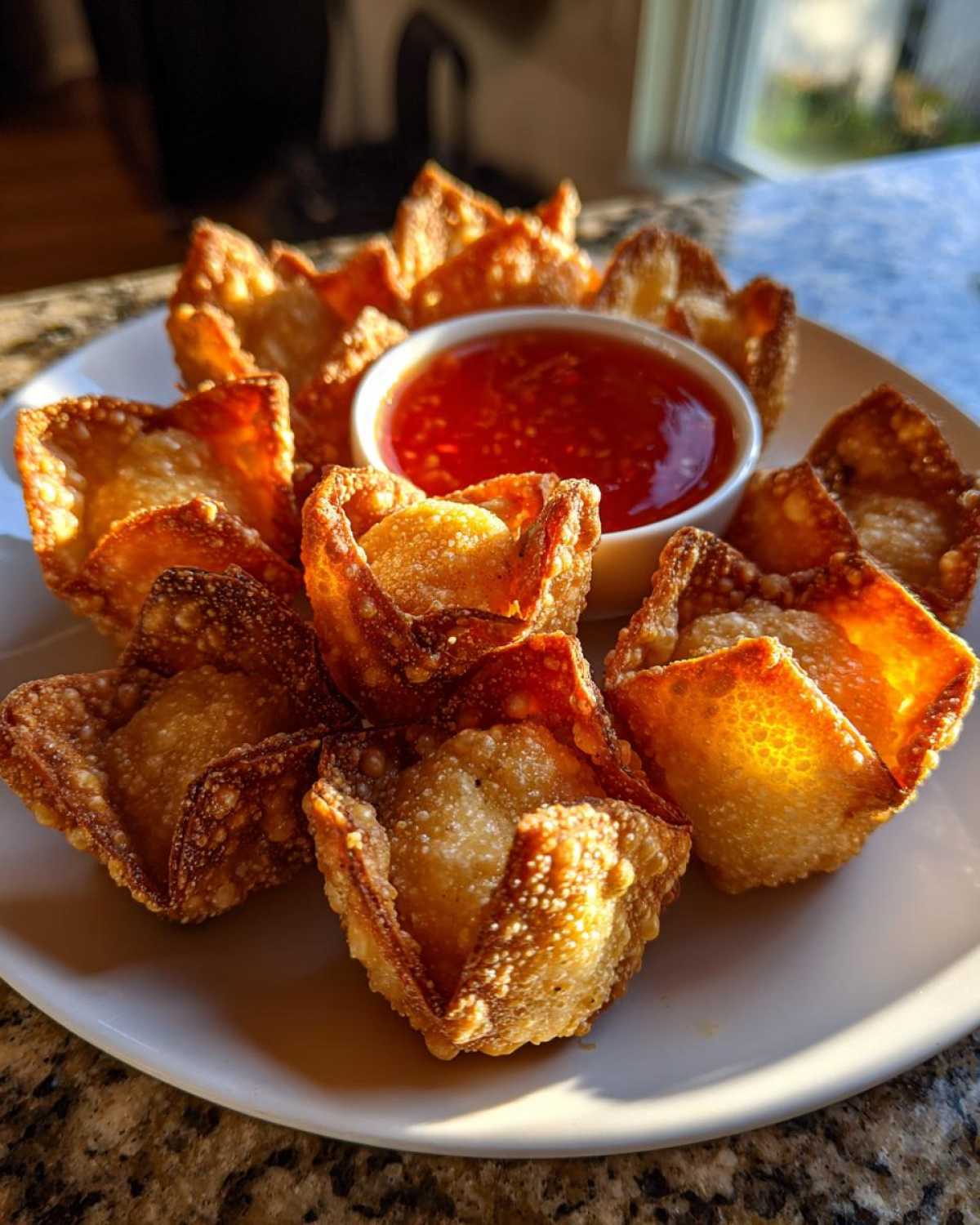A plate of freshly fried, golden brown crab rangoon bombs arranged around a small bowl of sweet chili dipping sauce.