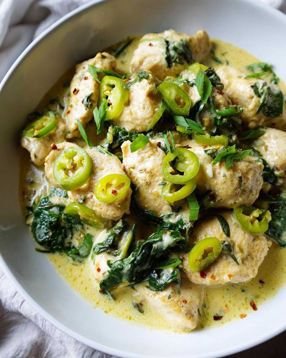 Close-up of creamy banana pepper chicken skillet with spinach, garnished with bright green pepper rings.