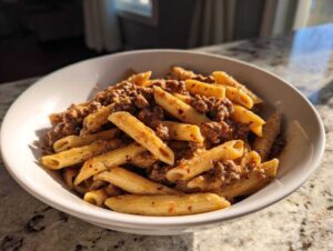A close-up of creamy beef pasta made with penne noodles and ground beef sauce, served in a white bowl.