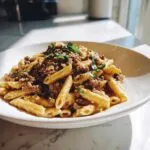 A close-up of a bowl filled with creamy beef pasta made with penne noodles and topped with fresh herbs.