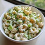 A white bowl filled with creamy cottage cheese pasta salad featuring ring-shaped pasta, chunks of celery, and topped with fresh chives.