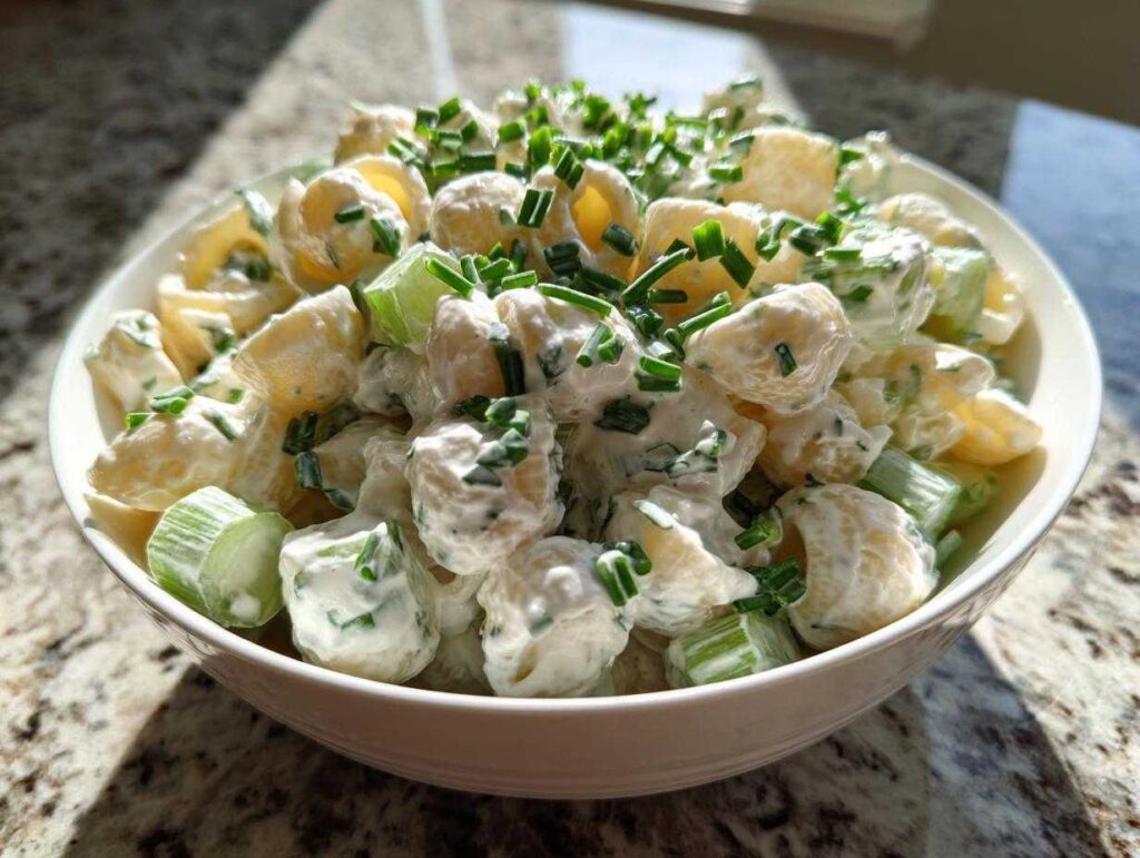 Close-up of a bowl filled with creamy cottage cheese pasta salad mixed with chopped celery and topped with fresh chives.
