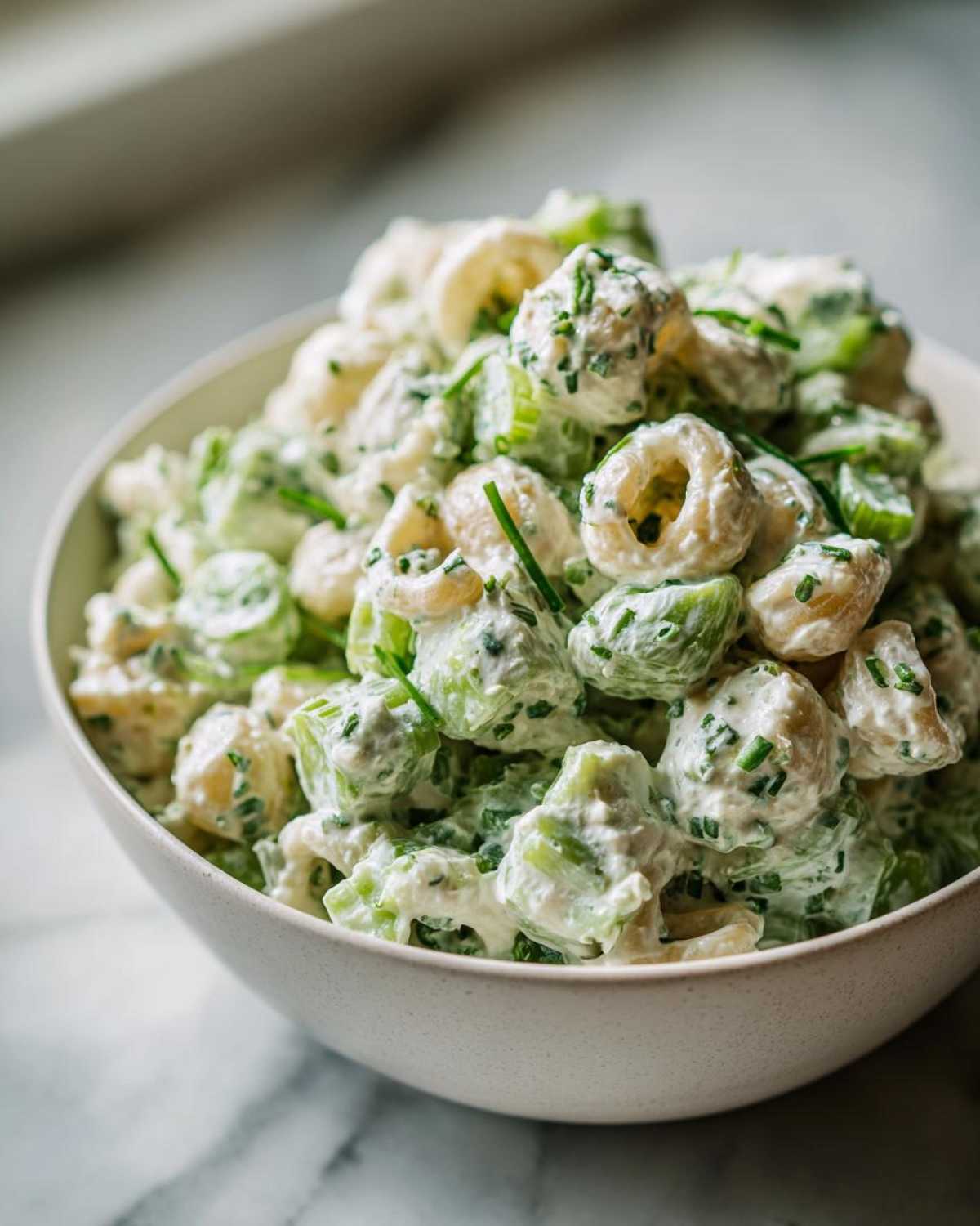 Close-up of a creamy cottage cheese pasta salad mixed with celery and chives, served in a light-colored bowl.