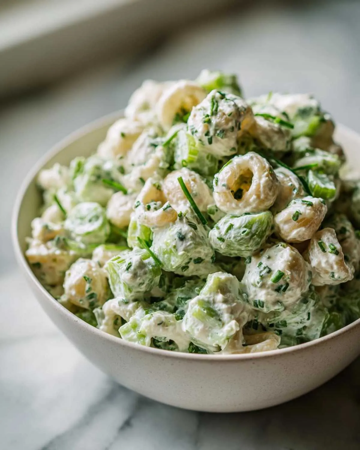 Close-up of a creamy cottage cheese pasta salad mixed with celery and chives, served in a light-colored bowl.