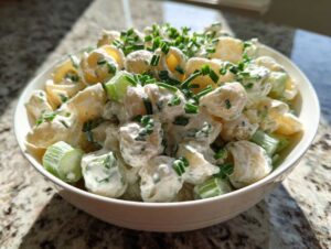 Close-up of a bowl filled with creamy cottage cheese pasta salad mixed with chopped celery and topped with fresh chives.