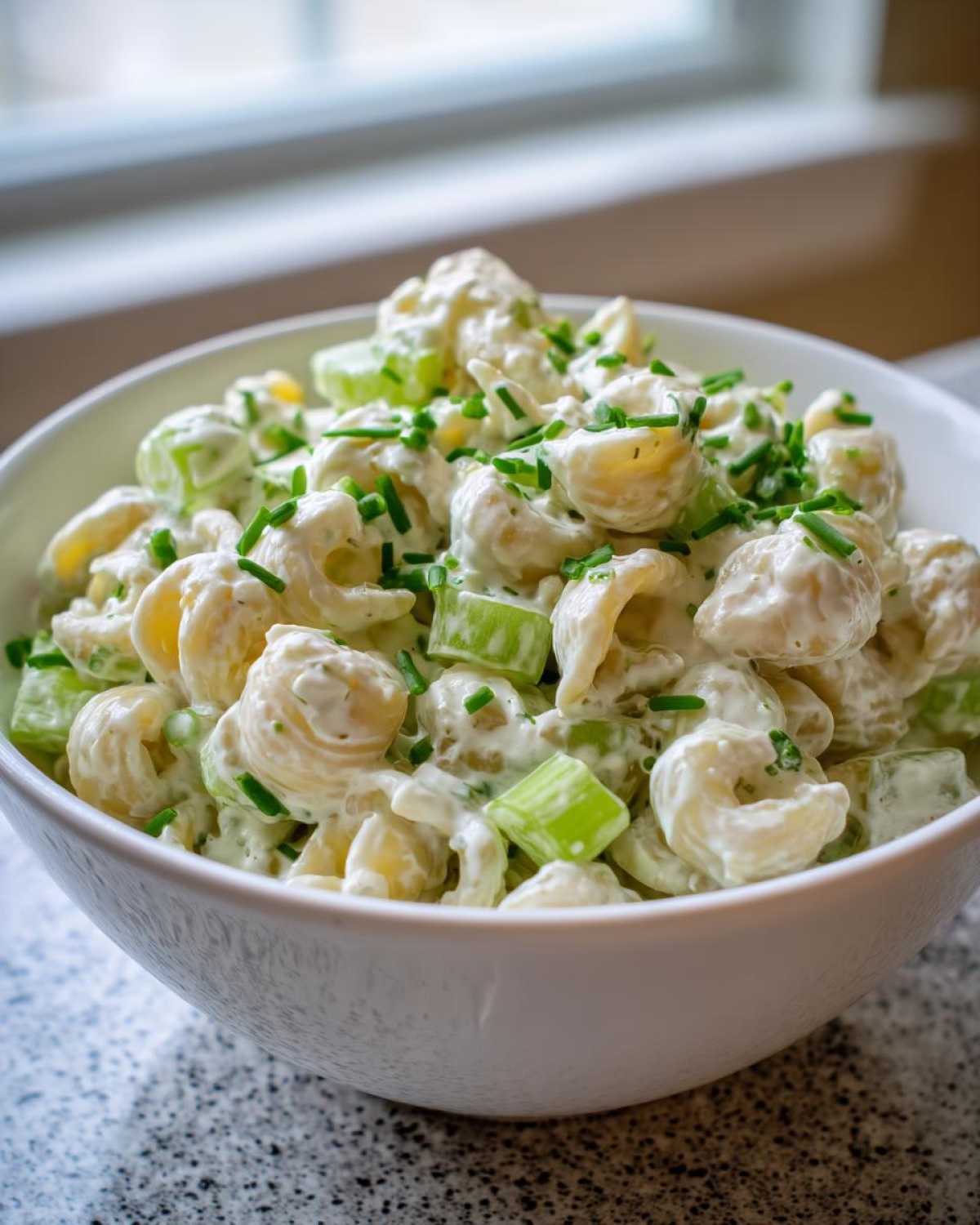 Close-up of creamy cottage cheese pasta salad with celery chunks and fresh chives topping.