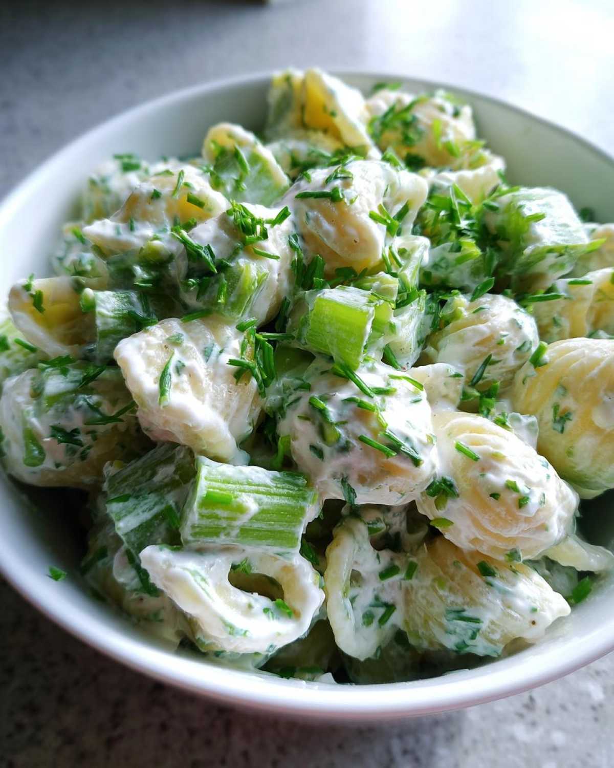 Close-up of a creamy cottage cheese pasta salad featuring shell pasta, chopped celery, and topped generously with fresh chives.