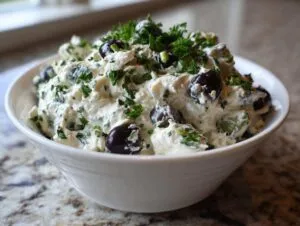A white bowl filled with creamy olive lovers dream dip, studded with black olives and topped with fresh parsley.