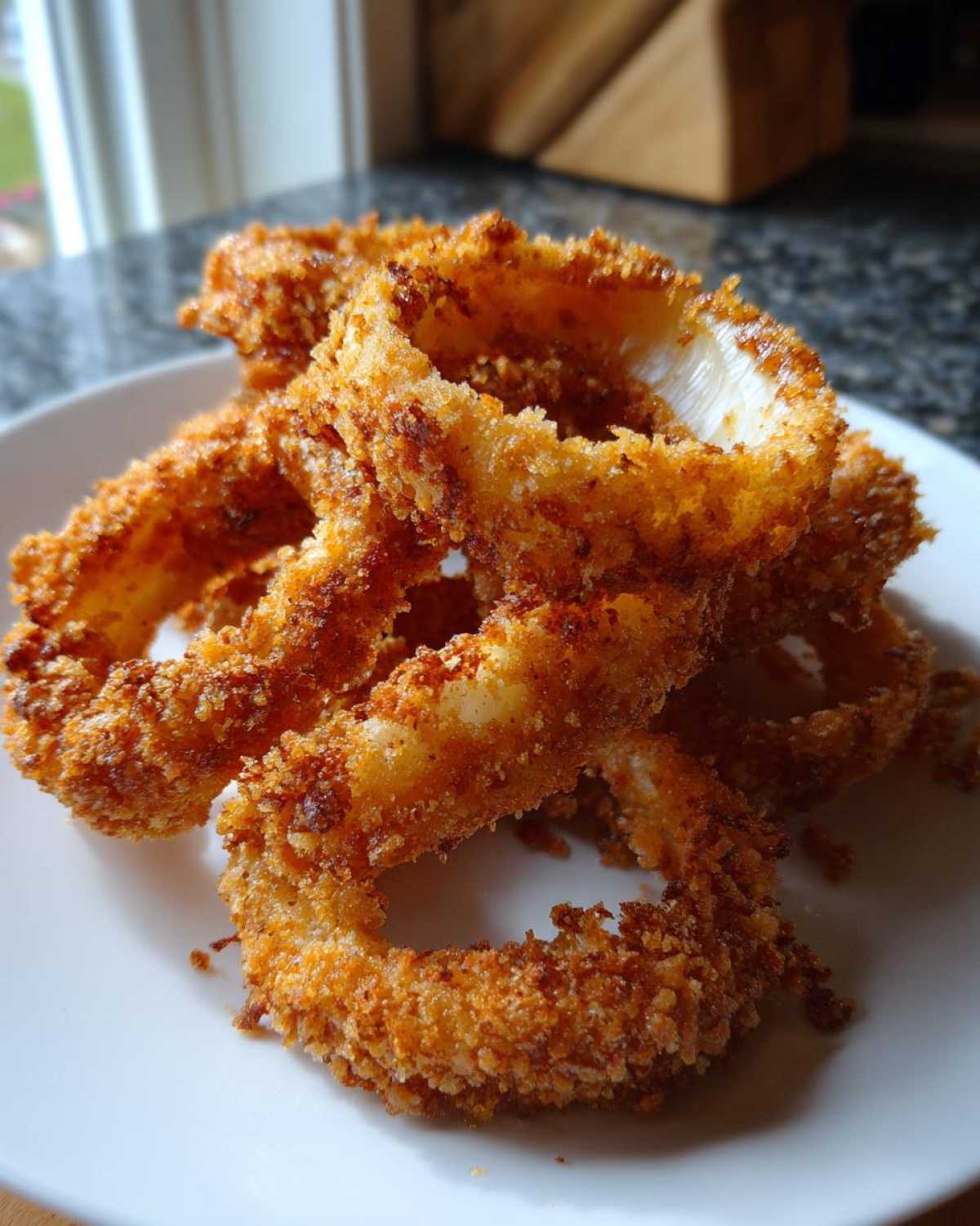 A close-up of several golden brown, crispy air fryer onion rings piled on a white plate.
