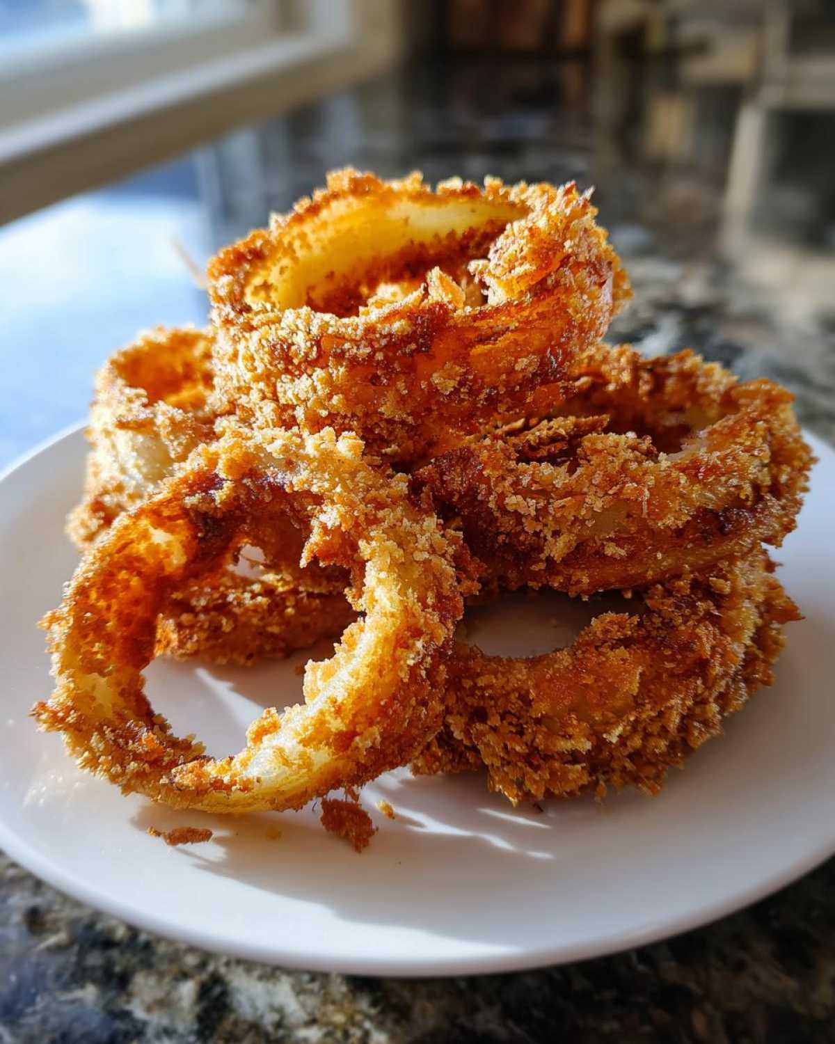 Close-up of several golden brown, crispy air fryer onion rings stacked on a white plate.