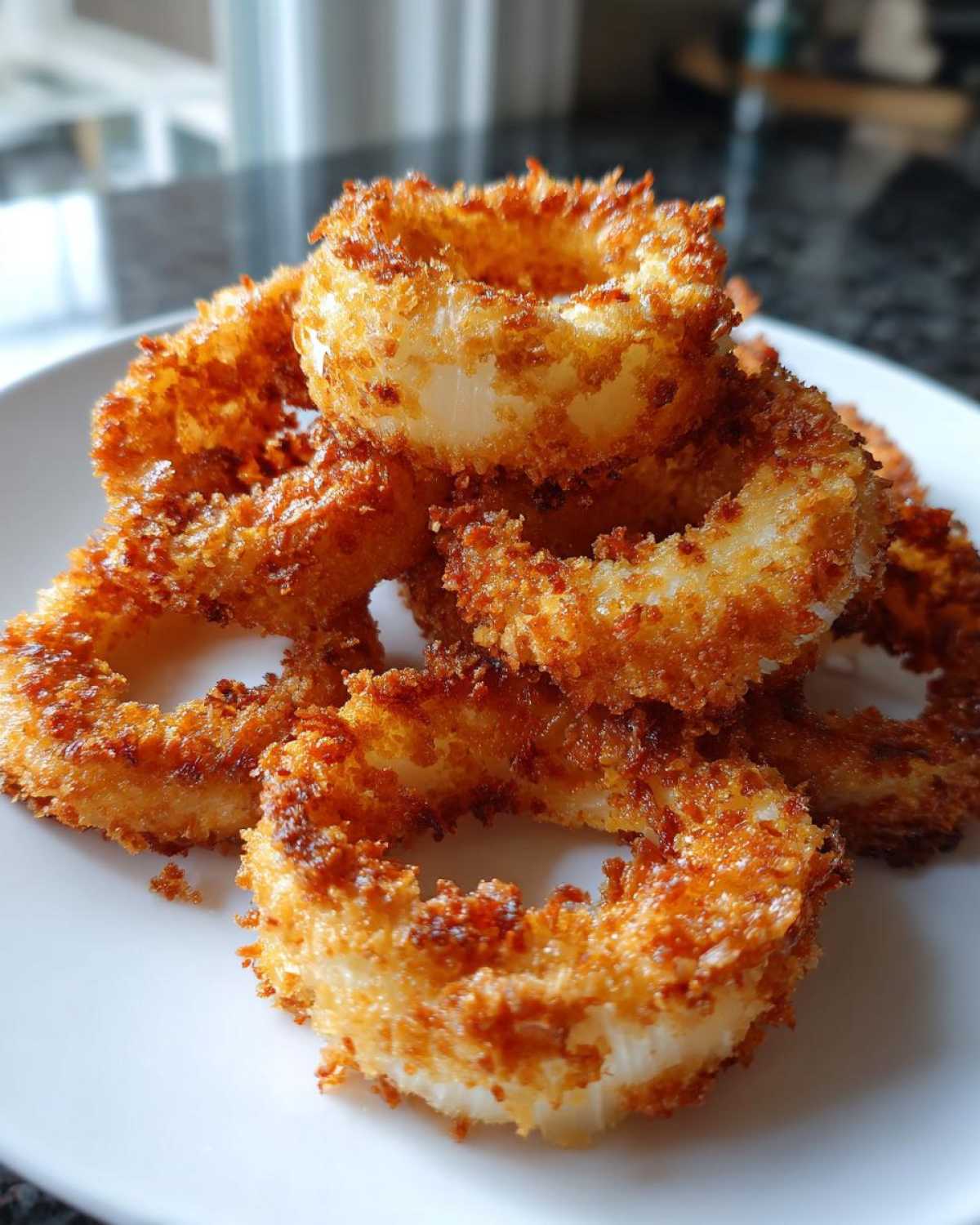 Close-up of a pile of golden brown, crispy air fryer onion rings stacked on a white plate.