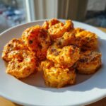 A pile of crispy, saucy Bang Bang Shrimp coated in a creamy orange sauce and sprinkled with dark herbs on a white plate.
