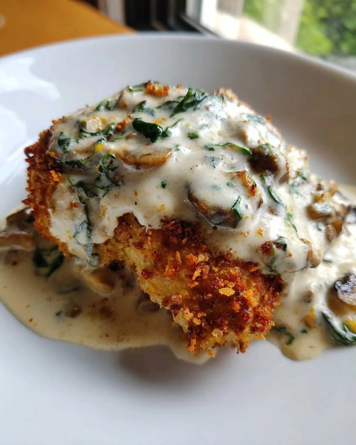 Close-up of crispy malibu chicken topped with a rich, creamy mushroom and spinach sauce.