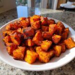 A white bowl filled with perfectly roasted, crispy, and seasoned sweet potatoes cubes.