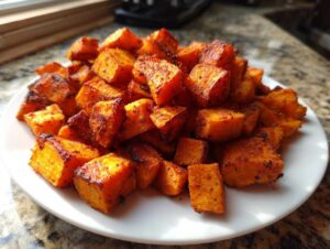 A close-up of perfectly roasted, crispy sweet potatoes cubes piled high on a white plate.