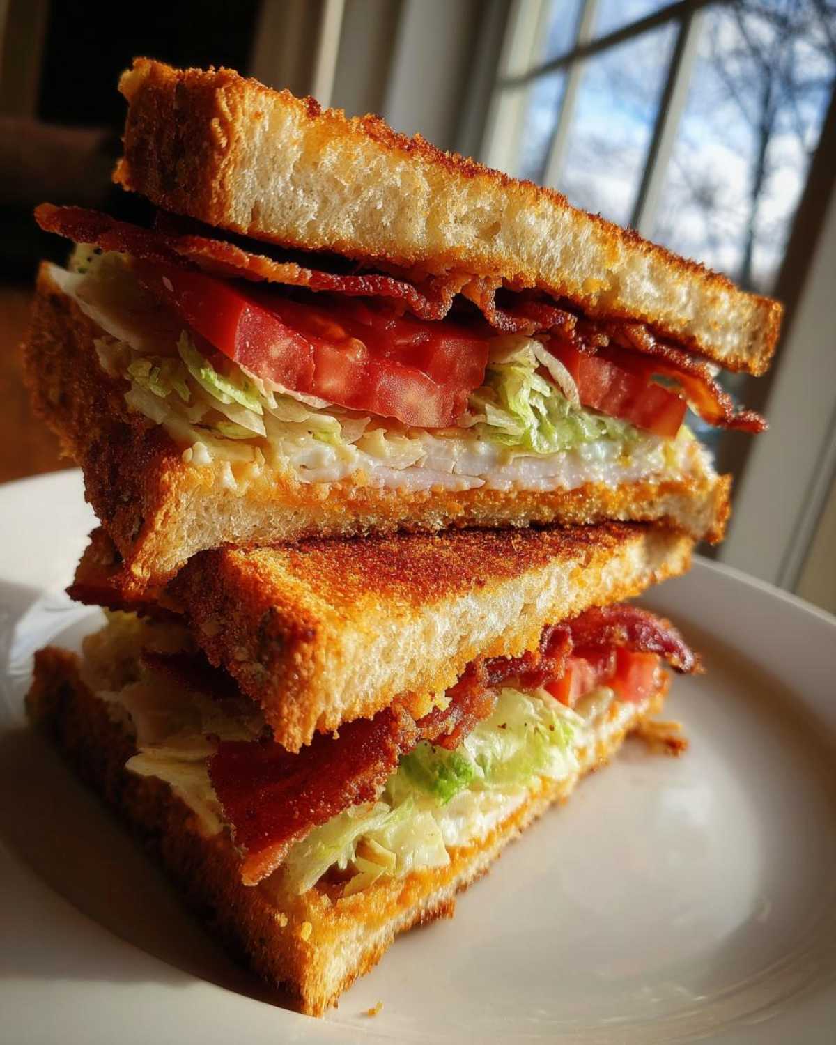 A tall, stacked crispy ultimate club sandwich cut in half, showing layers of toasted bread, bacon, tomato, and lettuce.