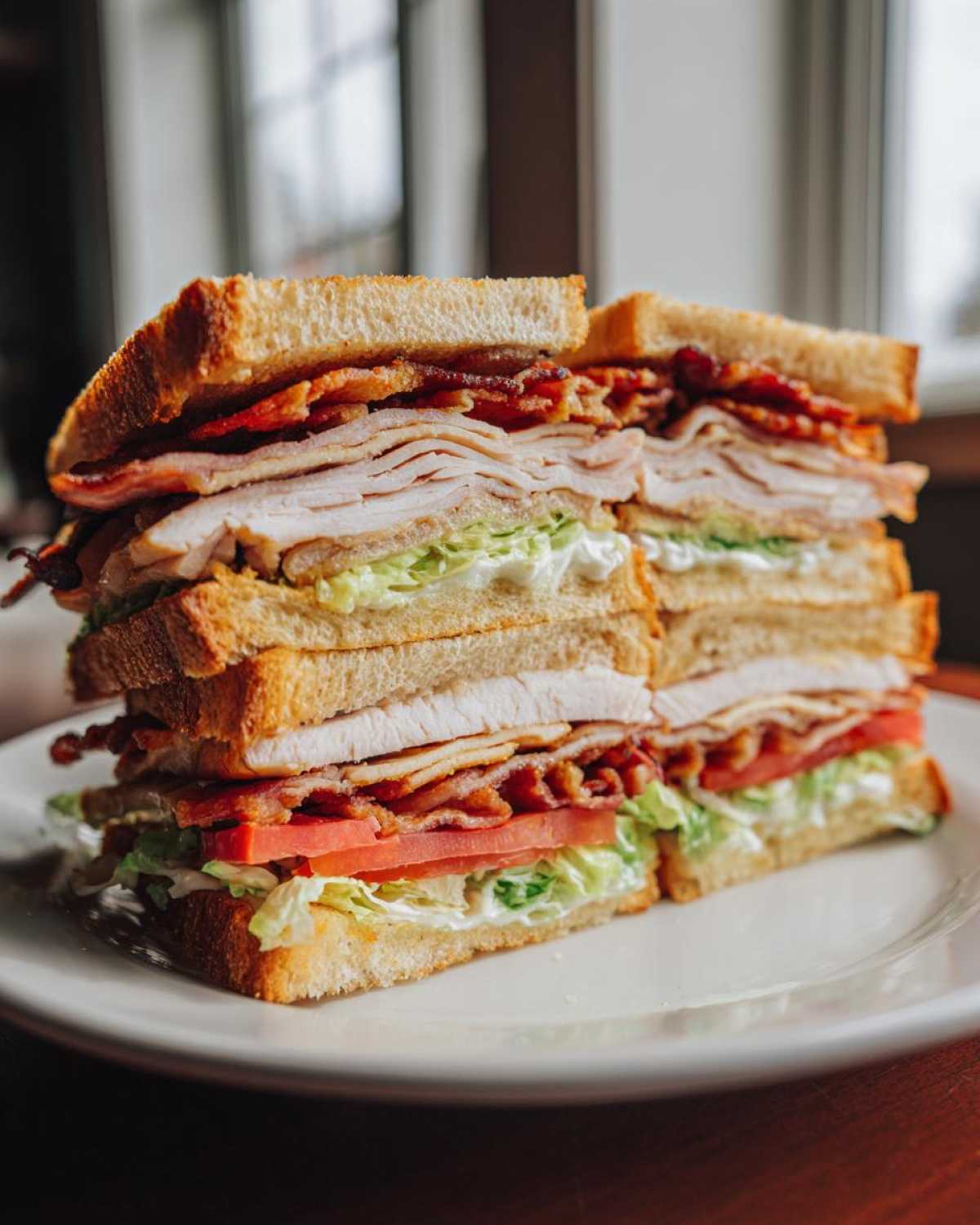 A towering, cross-section view of a crispy ultimate club sandwich showing layers of toasted bread, turkey, bacon, lettuce, and tomato.