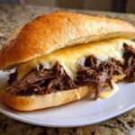 Close-up of a hearty crockpot french dip sandwiches filled with shredded beef and melted provolone cheese on a toasted roll.