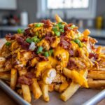 A towering serving of dirty chicken and bacon loaded fries smothered in melted cheese sauce and topped with green onions.