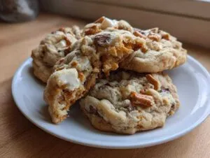 A stack of three amazing kitchen sink cookies, one broken open to show white chocolate chunks and pretzels.