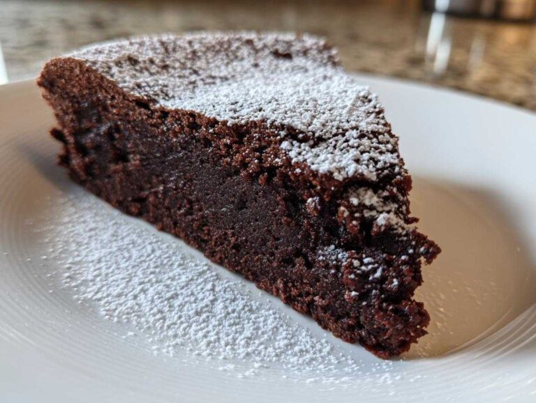 A close-up of a rich, dense slice of flourless chocolate cake dusted generously with powdered sugar on a white plate.