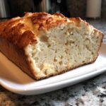 Close-up of a freshly baked beer bread loaf sliced open, showing a soft interior and golden crust.
