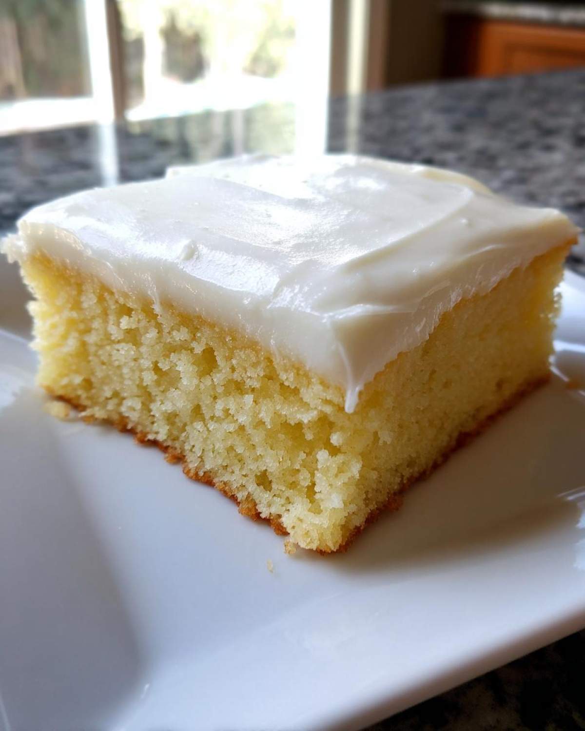 Close-up of a thick, square slice of yellow sugar cookie bars topped with smooth white frosting.