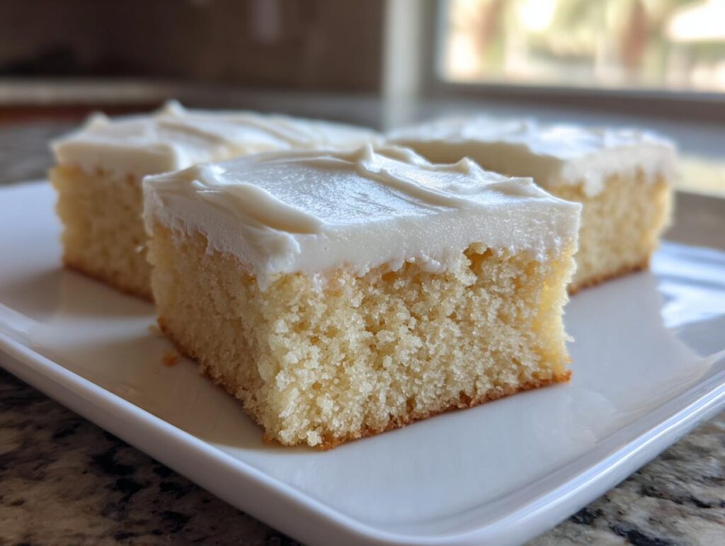 Three square slices of soft, pale yellow sugar cookie bars topped with thick white frosting.