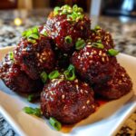 Close-up of sticky, glazed korean bbq meatballs topped with sesame seeds and chopped green onions.
