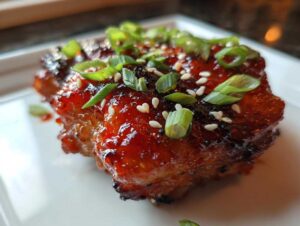 Close-up of a piece of glazed sweet chili chicken, topped with sliced green onions and sesame seeds.