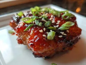 Close-up of a piece of glazed sweet chili chicken, topped with sliced green onions and sesame seeds.