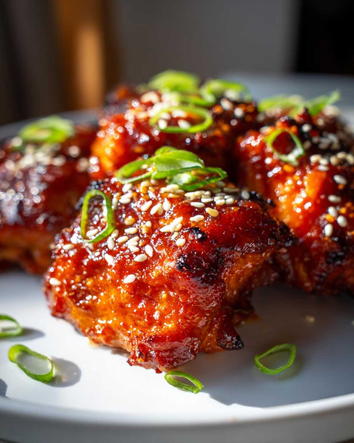 Close-up of sticky, glazed sweet chili chicken pieces topped with sesame seeds and sliced green onions.