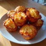 A pile of golden brown, freshly baked pancake poppers served on a white plate under natural light.