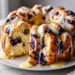 A close-up of a slice being pulled from a ring of gooey blueberry monkey bread drizzled with vanilla glaze.