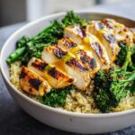 A close-up of a healthy grilled chicken and broccoli bowls featuring sliced grilled chicken over quinoa and green broccoli.