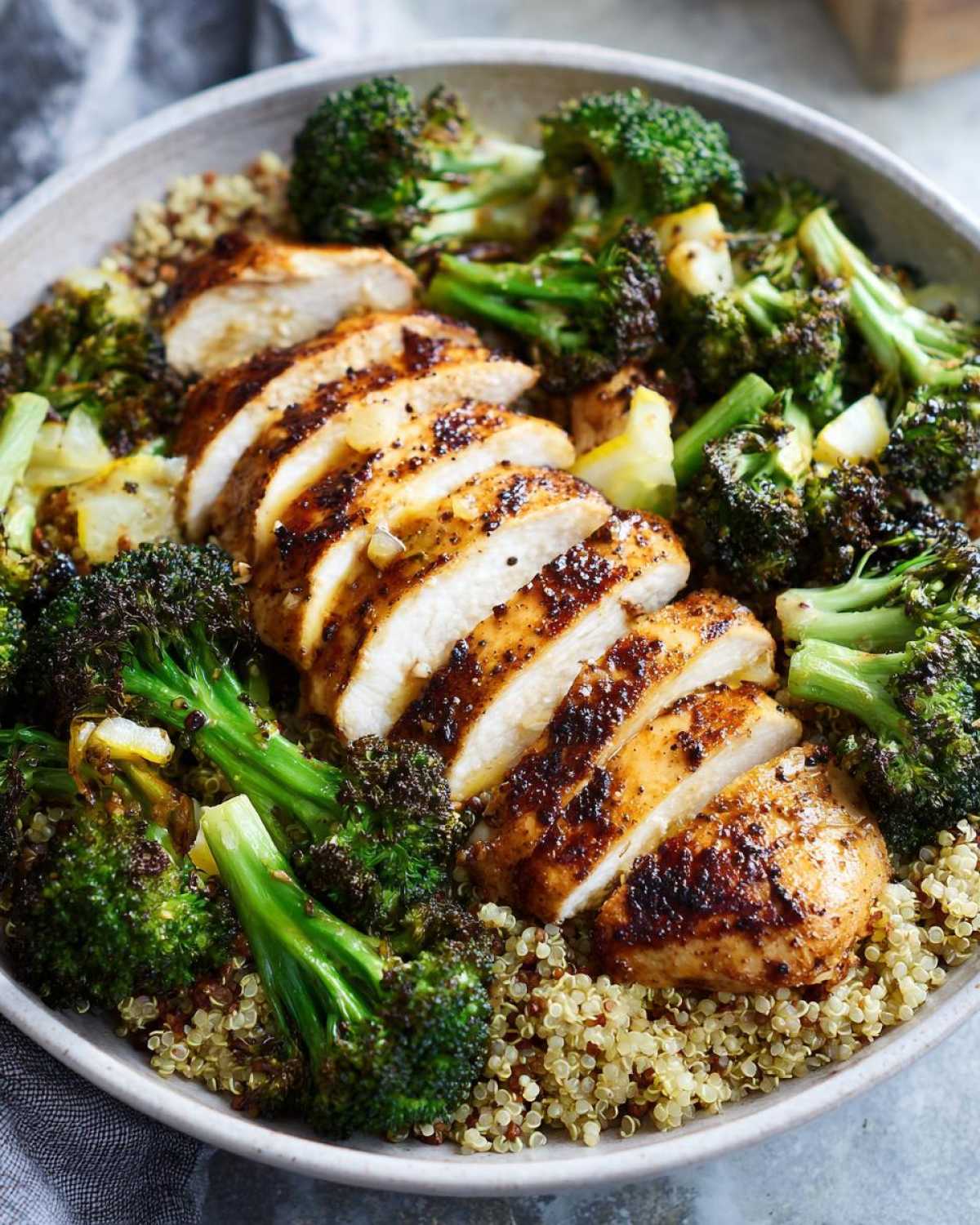 Close-up of a bowl featuring sliced grilled chicken and roasted broccoli served over a bed of quinoa for grilled chicken and broccoli bowls.